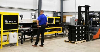 Person operating factory equipment with a forklift in the background.